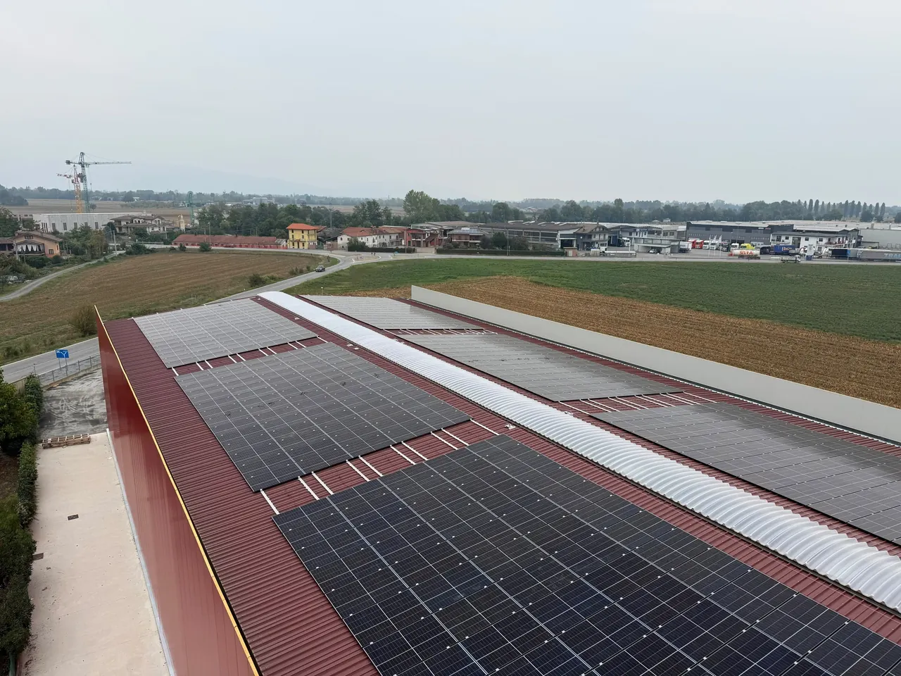 Vista lungo il tetto in lamiera rossa di un grande edificio, con campi di moduli fotovoltaici e una fascia ondulata chiara al centro
