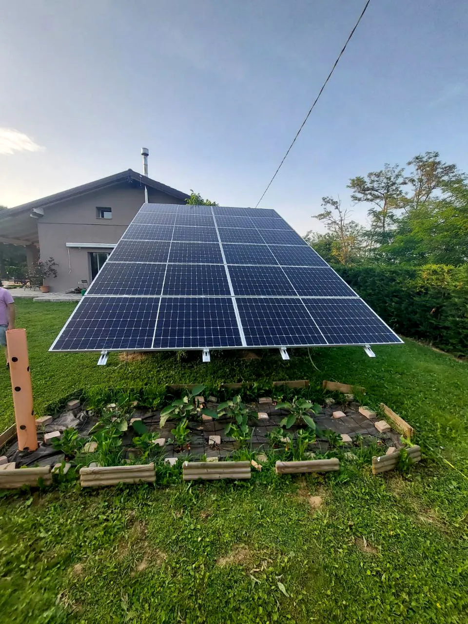 Moduli fotovoltaici su una struttura inclinata appoggiata al prato, accanto a un edificio con tetto a falde