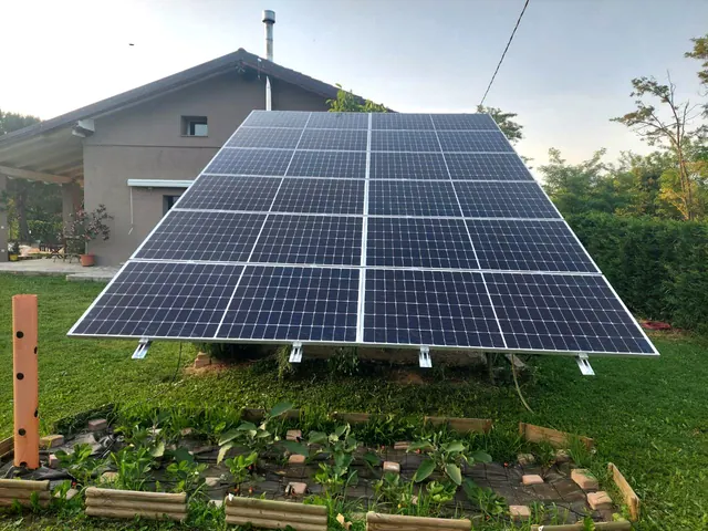 Struttura a terra con moduli fotovoltaici vista da un lato, tra aiuole coltivate e un edificio sullo sfondo