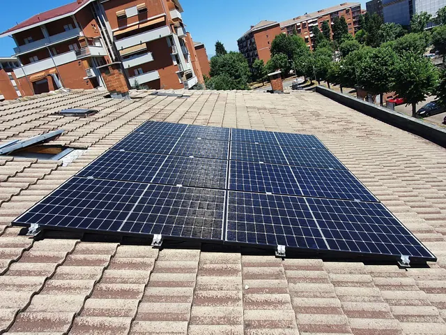 Moduli fotovoltaici su un tetto a falde in tegole, con palazzi residenziali e alberi sullo sfondo