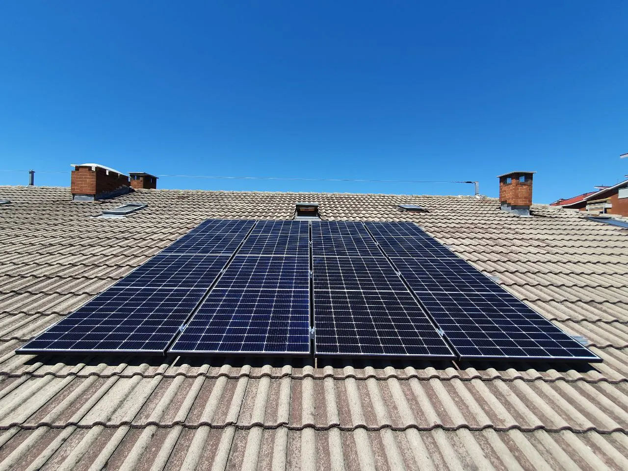 Moduli fotovoltaici su un tetto in tegole con camini, visti dal bordo della falda