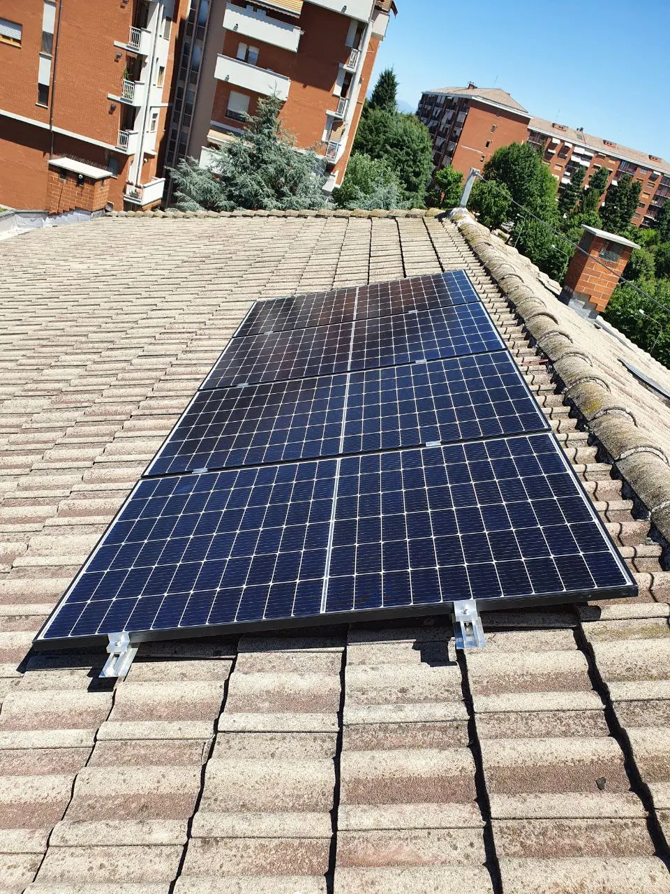 Moduli fotovoltaici fissati con staffe su una falda in tegole, con palazzi sullo sfondo