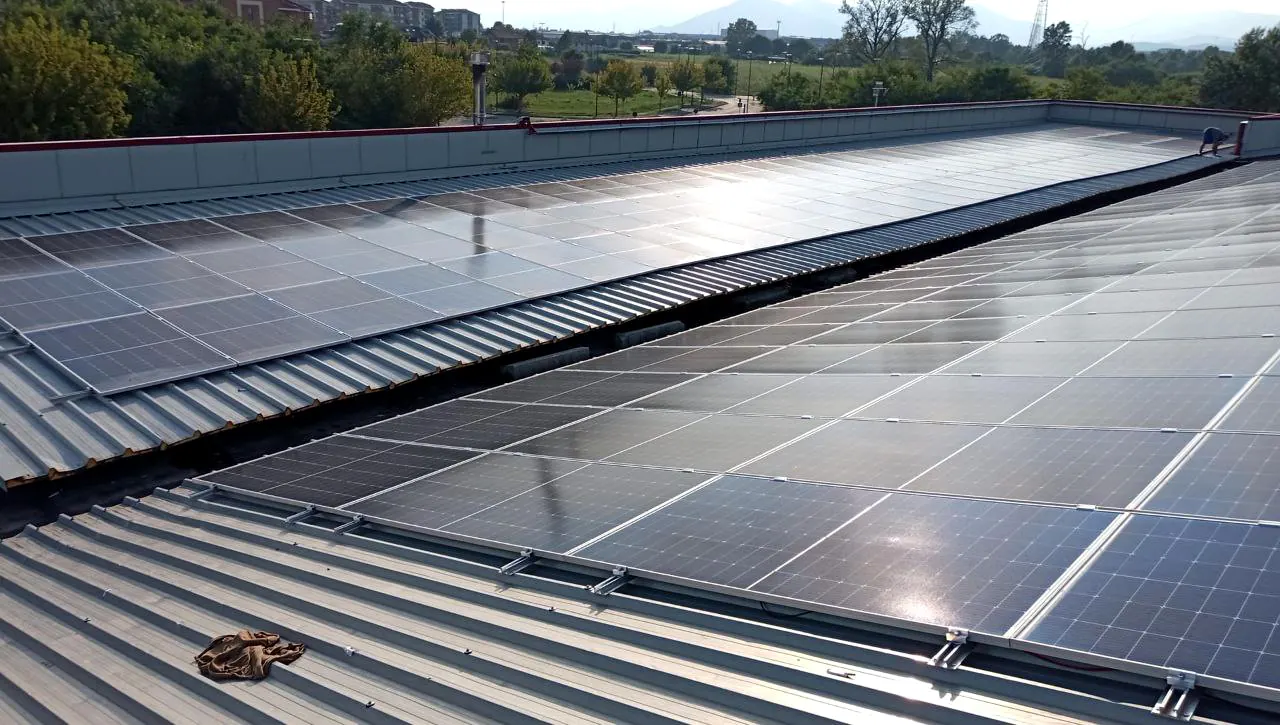 Moduli fotovoltaici in file ravvicinate lungo una copertura in lamiera grecata, visti dal bordo del tetto