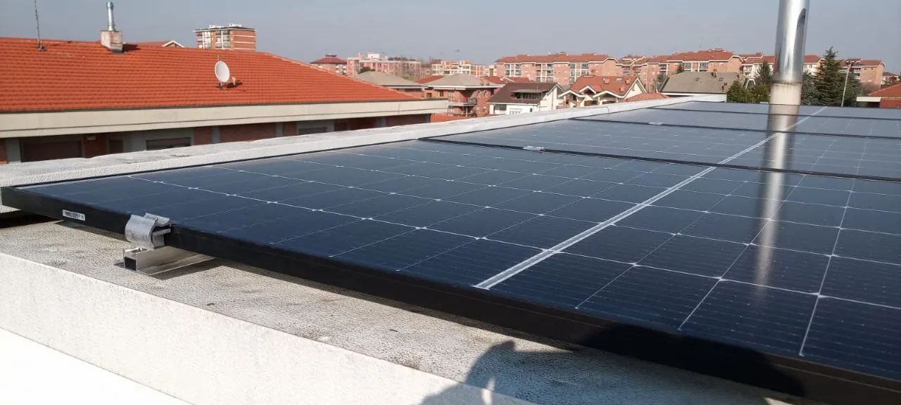 Moduli fotovoltaici lungo il bordo di una copertura chiara, con tetti in tegole sullo sfondo